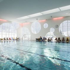 an indoor swimming pool with lots of windows and people sitting on the benches in it