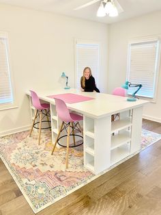 a woman sitting at a white table in a room with pink chairs and a rug on the floor