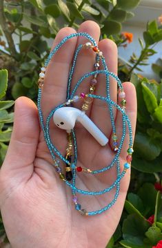 a hand holding an earbud with beads on it in front of some plants