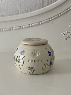 a white vase with blue flowers and the words bailey painted on it's side