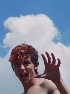 a man with red hair is holding his hands up in front of the sky and clouds