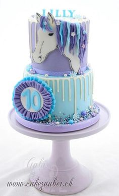 two tiered cake decorated with blue and purple icing and a horse on top