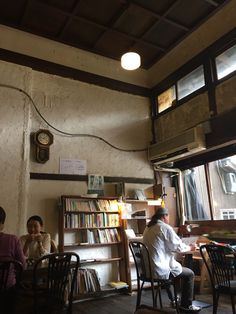 two people sitting at a table in front of a book shelf with books on it