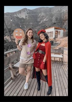 two women dressed in costumes posing for a photo on a wooden deck with mountains in the background