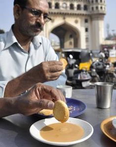 a man sitting at a table with food in front of him and another person eating