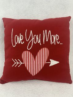 a red pillow that says love you more with an arrow and heart on the front