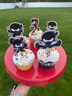 cupcakes with sprinkles and cartoon characters on them sitting on a red plate