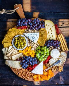 a platter filled with cheese, crackers, grapes, nuts and olives