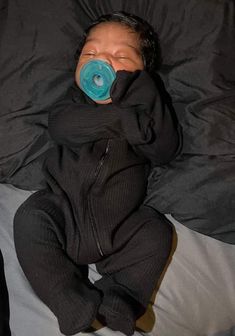 a baby with a pacifier in its mouth laying on a bed