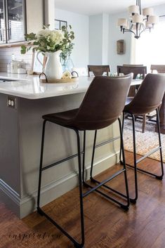 a kitchen island with four stools in front of it and a vase on the counter