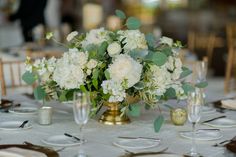 a vase filled with white flowers sitting on top of a table next to plates and silverware