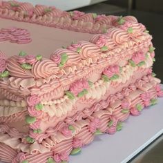 a large cake with pink frosting and green leaves on it's edges is sitting on a table