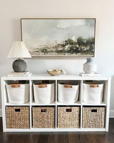 a white shelf with baskets on it and a painting hanging above the shelves in front of it