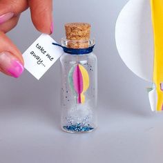 a hand holding a tiny bottle with a hot air balloon in it and a note attached to the top