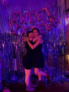 two women hugging each other in front of balloons and streamers with the word sweet on it