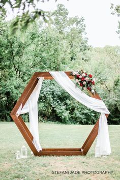 a wedding arch with white draping and red flowers on the top is surrounded by greenery