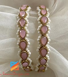 two pink and white bracelets on top of a white cloth with gold trimming