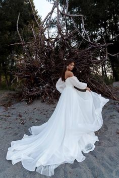 a woman in a white dress is standing on the sand with her arms around her back