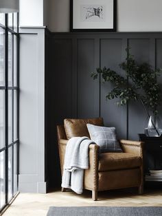 a living room with black paneling and leather chair next to a potted plant