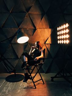 a woman sitting in a chair next to a light on a tripod with lights behind her