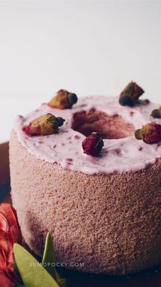 a cake with frosting and berries on top sitting on a plate next to flowers