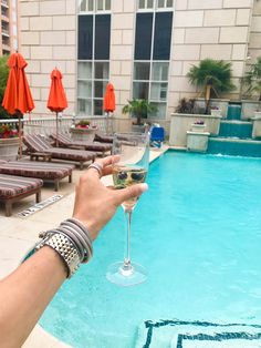 a person holding a wine glass in front of a swimming pool