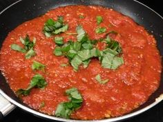 a pan filled with sauce and herbs on top of a stove