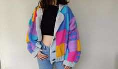 a woman standing in front of a white wall wearing a colorful sweater and ripped jeans