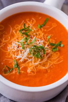 a white bowl filled with tomato soup topped with parmesan cheese and green garnish