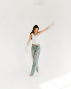 a woman in white shirt and jeans dancing with her arms spread out to the side