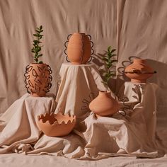 four clay vases with plants in them on a cloth covered tableclothed surface