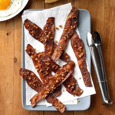 bacon strips sitting on top of a white plate next to an egg and spoons