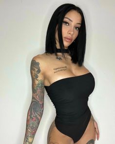 a woman in a black swimsuit with tattoos on her arms and legs, posing for the camera