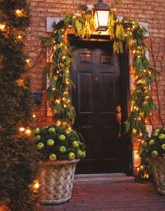 two planters filled with green apples sit in front of a door decorated for christmas