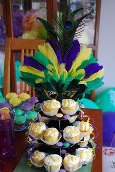 a table topped with cupcakes covered in frosting next to a peacock feather