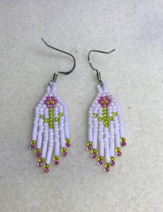 white beaded earrings with pink, green and yellow beads hanging from hooks on a table