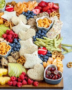 a wooden platter filled with fruit, crackers, and pretzels on top of a table