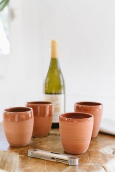 four clay cups sitting on top of a wooden table next to a bottle of wine