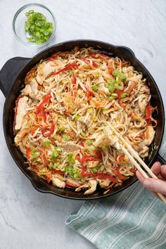 someone holding chopsticks over a skillet with chicken and noodles