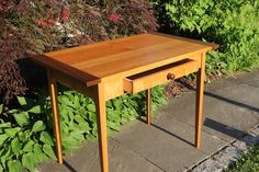 a small wooden table sitting on top of a sidewalk next to some bushes and flowers