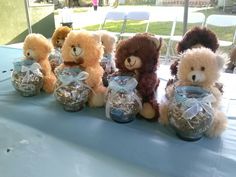 several stuffed animals are sitting in glass jars on a table with blue cloths and white chairs