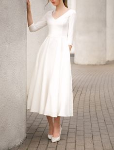 a woman in a white dress leaning against a wall