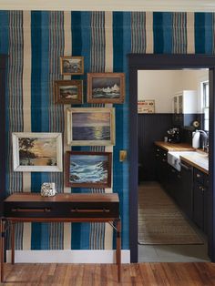 a room with blue and white striped wallpaper, wooden flooring and artwork on the walls