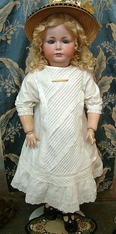 a doll with blonde hair wearing a white dress and hat