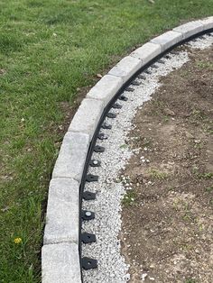 a train track in the middle of some grass and dirt on top of gravel, next to a grassy area