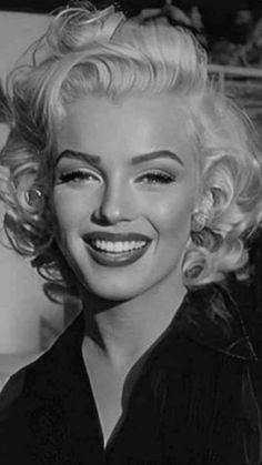 a black and white photo of a woman with blonde hair smiling at the camera,