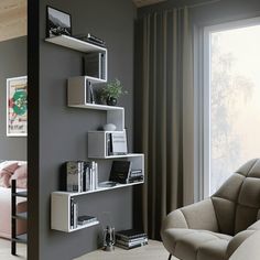 a living room filled with furniture next to a window and a wall mounted book shelf