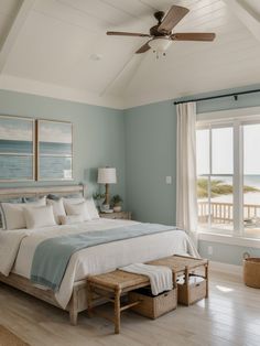 a bedroom with blue walls and white bedding in front of a large window overlooking the ocean