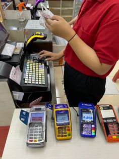 a woman standing at a cash register with several different types of cell phones next to her