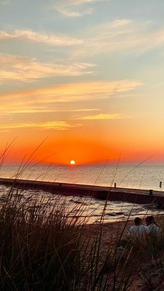 the sun is setting over the ocean and people are sitting on the beach near the water